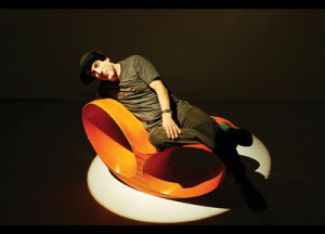 Ron Arad, wearing his trademark Cappellone, on an orange Oh-Void chair.