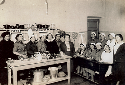 Fania Lewando stands between two tables at her renowned cooking school. Excerpted from ‘THE VILNA VEGETARIAN cookbook’ by Fania Lewando. © 2015 by Random House. Excerpted by permission of Schocken, a division of Random House LLC. All rights reserved.